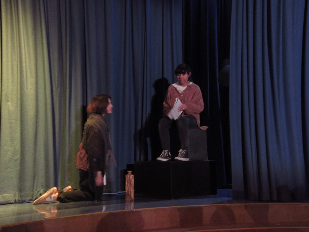 Caliban (Arianna Zalzalah) kneeling in-front of a sitting Stephano (Zaira Rodriguez).