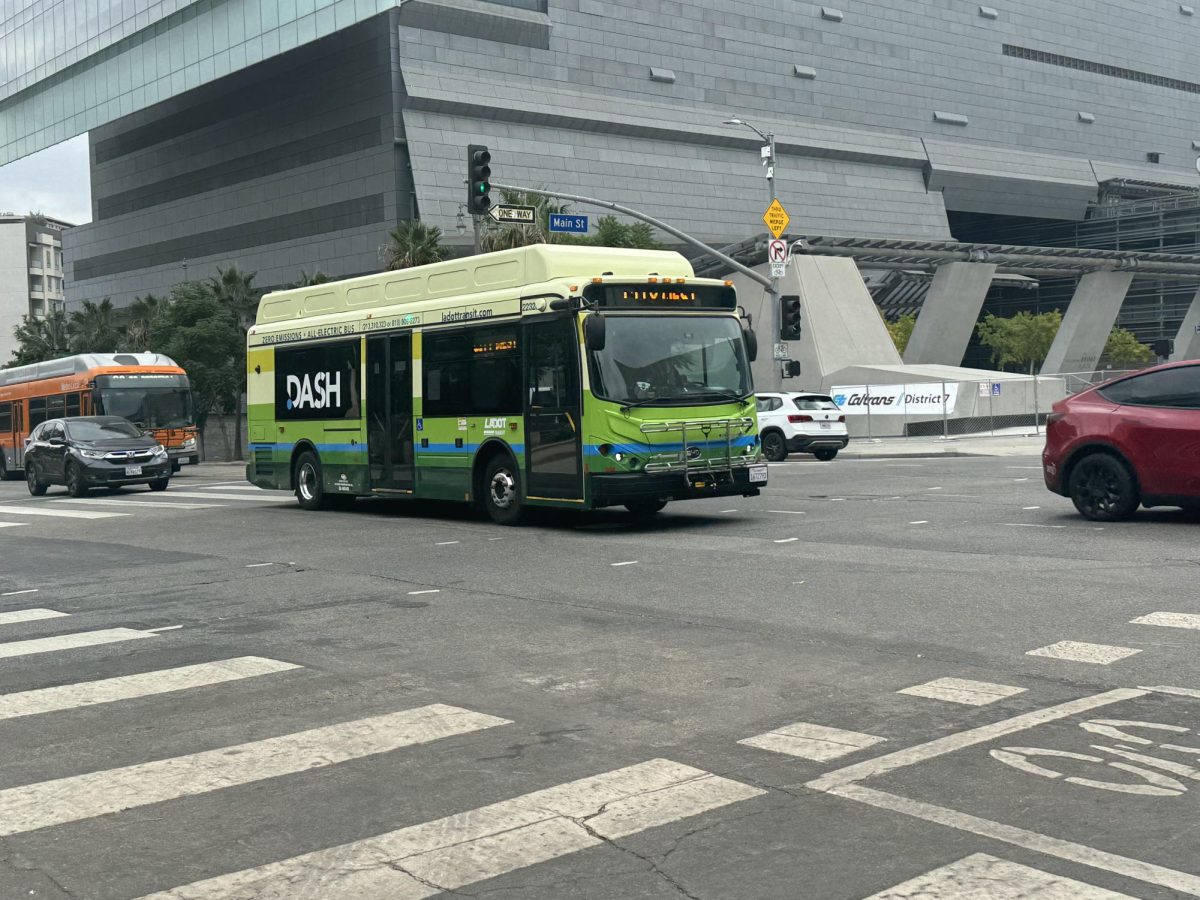 A Dash-operated zero-emissions battery bus in the foreground with a Los Angeles Metro Compressed Natural Gas bus emitting pollutants in the background.